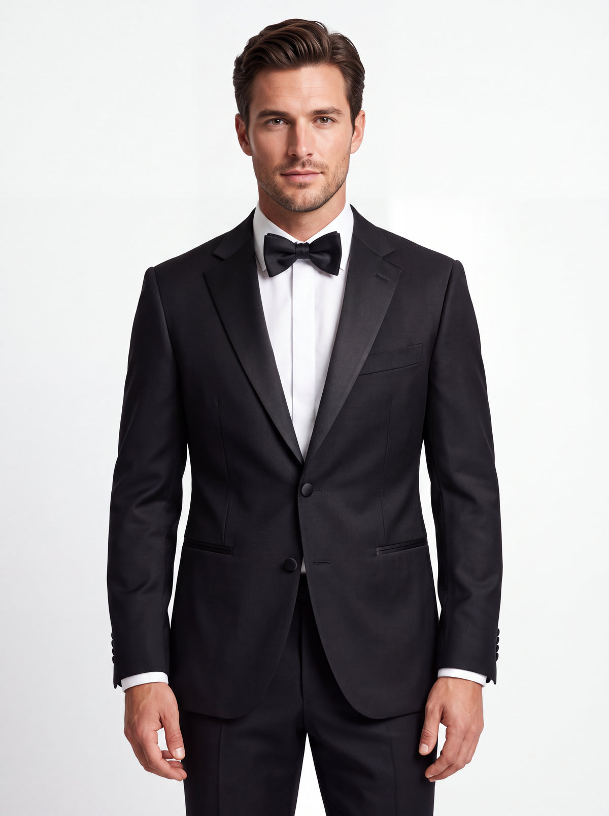 A man wearing a classic black tuxedo jacket with satin lapels, a white dress shirt, and a black bow tie, photographed against a clean white studio background.